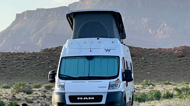 Two dogs alongside a campervan in front of a hidden gem desert landscape outside of Utah's national parks