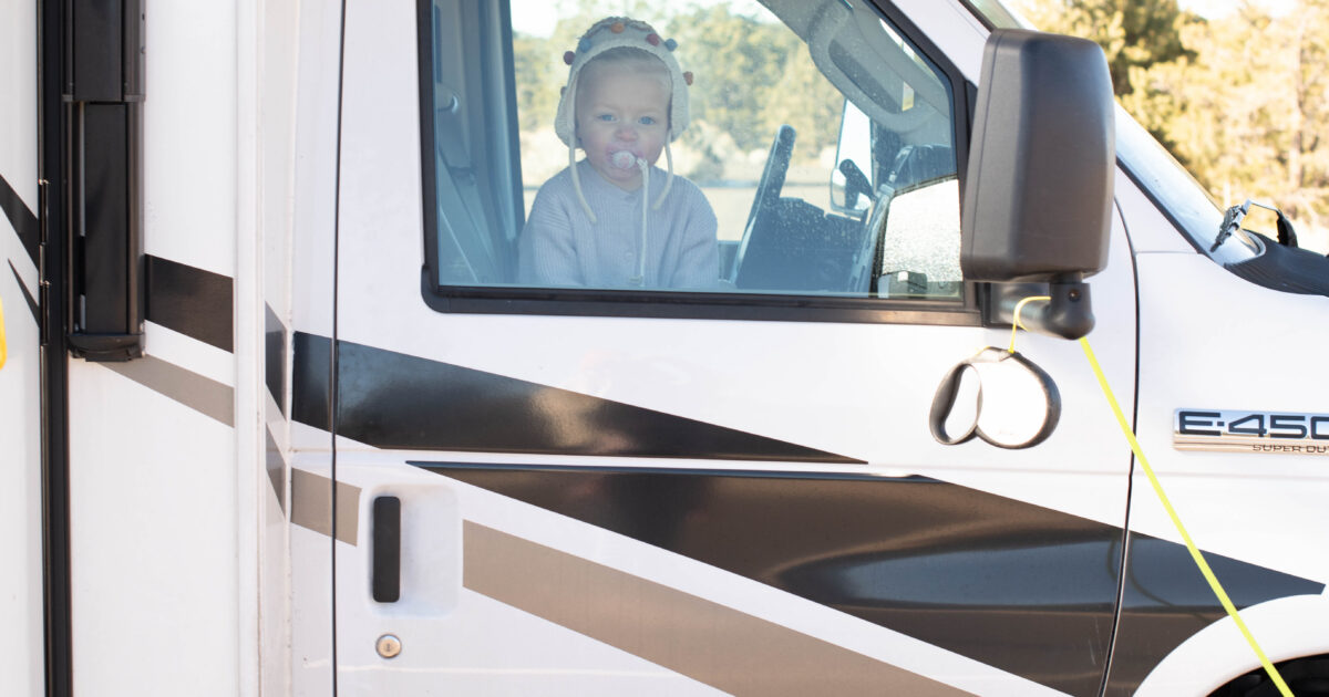 A toddler peers out of the passenger-side window of a Class C RV