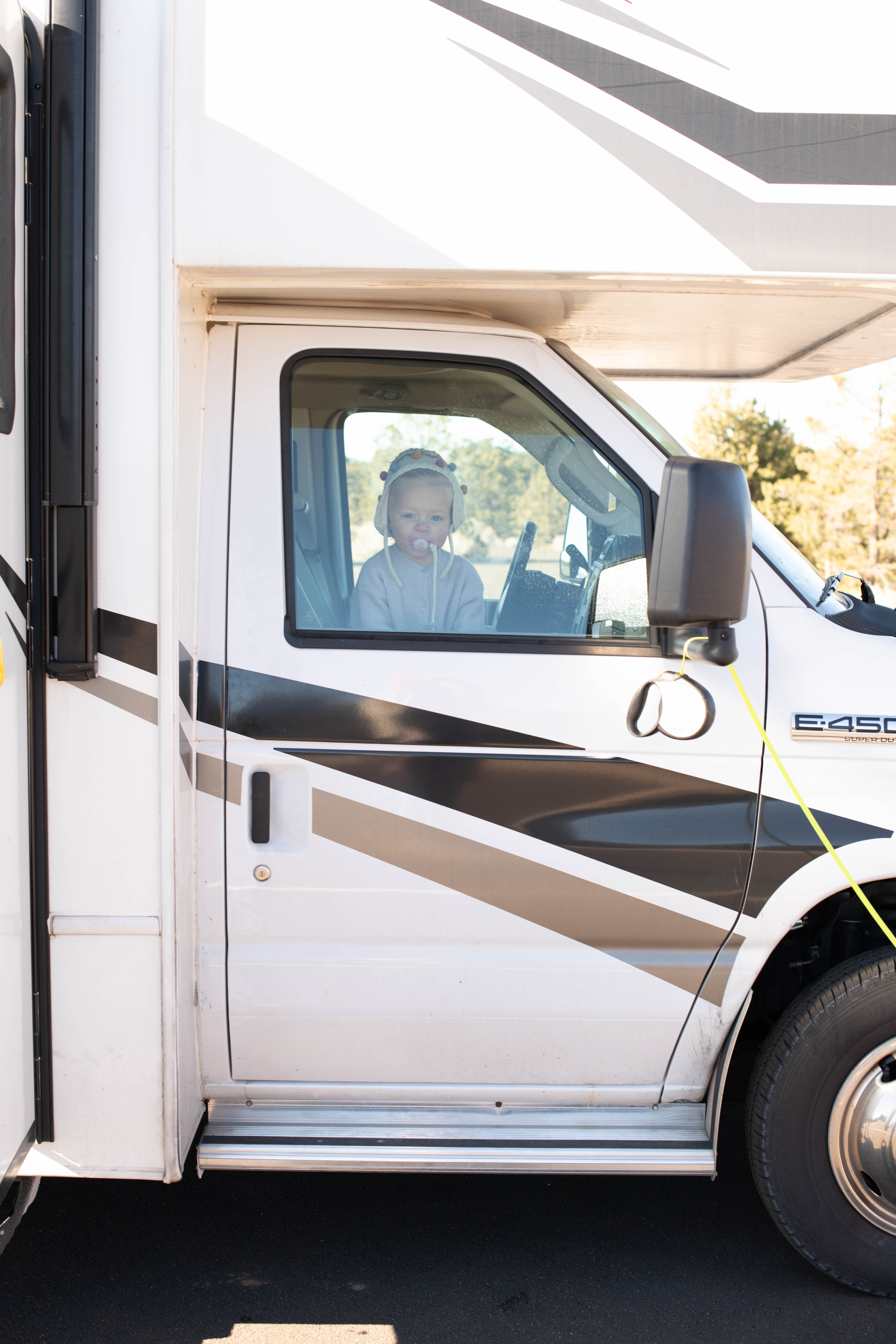 A toddler peers out of the passenger-side window of a Class C RV