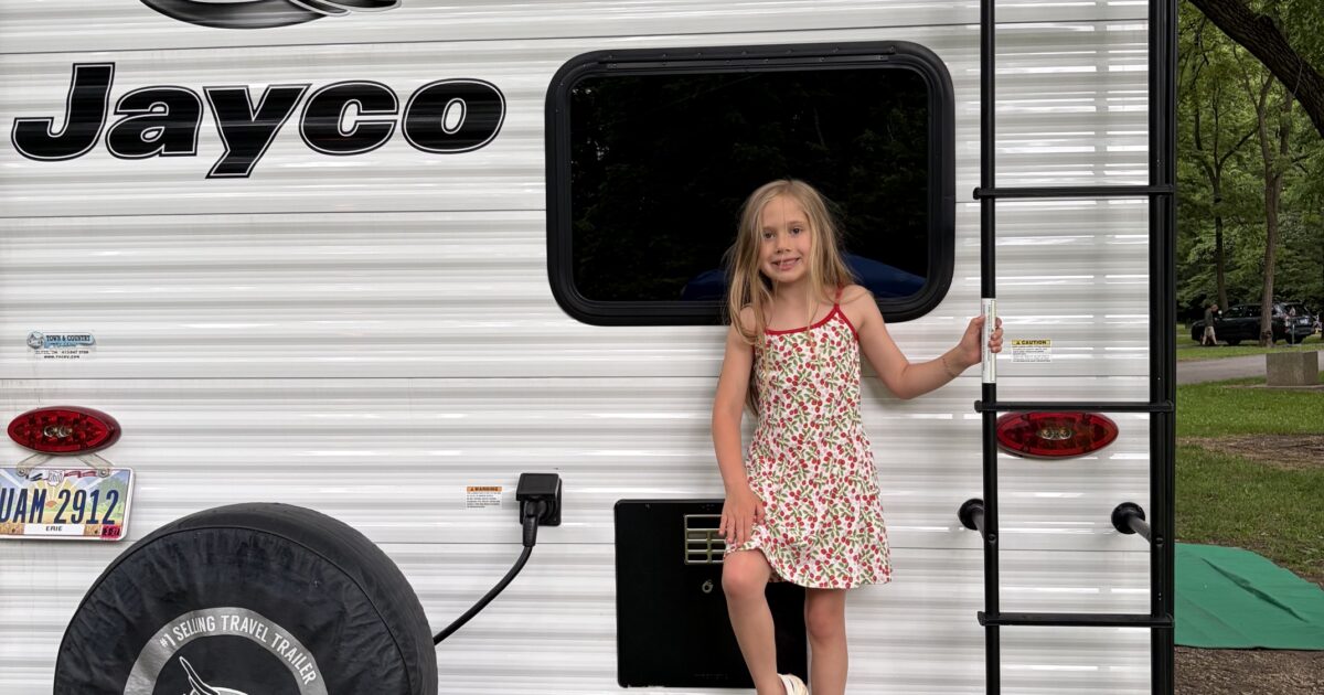 little girl standing on the back of a jayco travel trailer