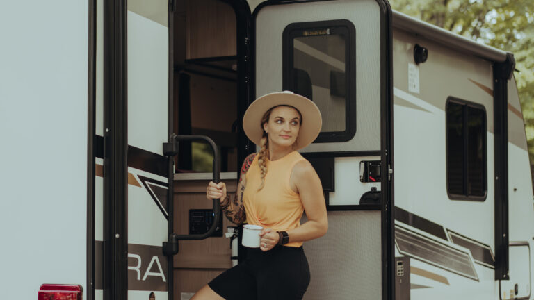 A woman walks up the steps into her travel trailer, smiling