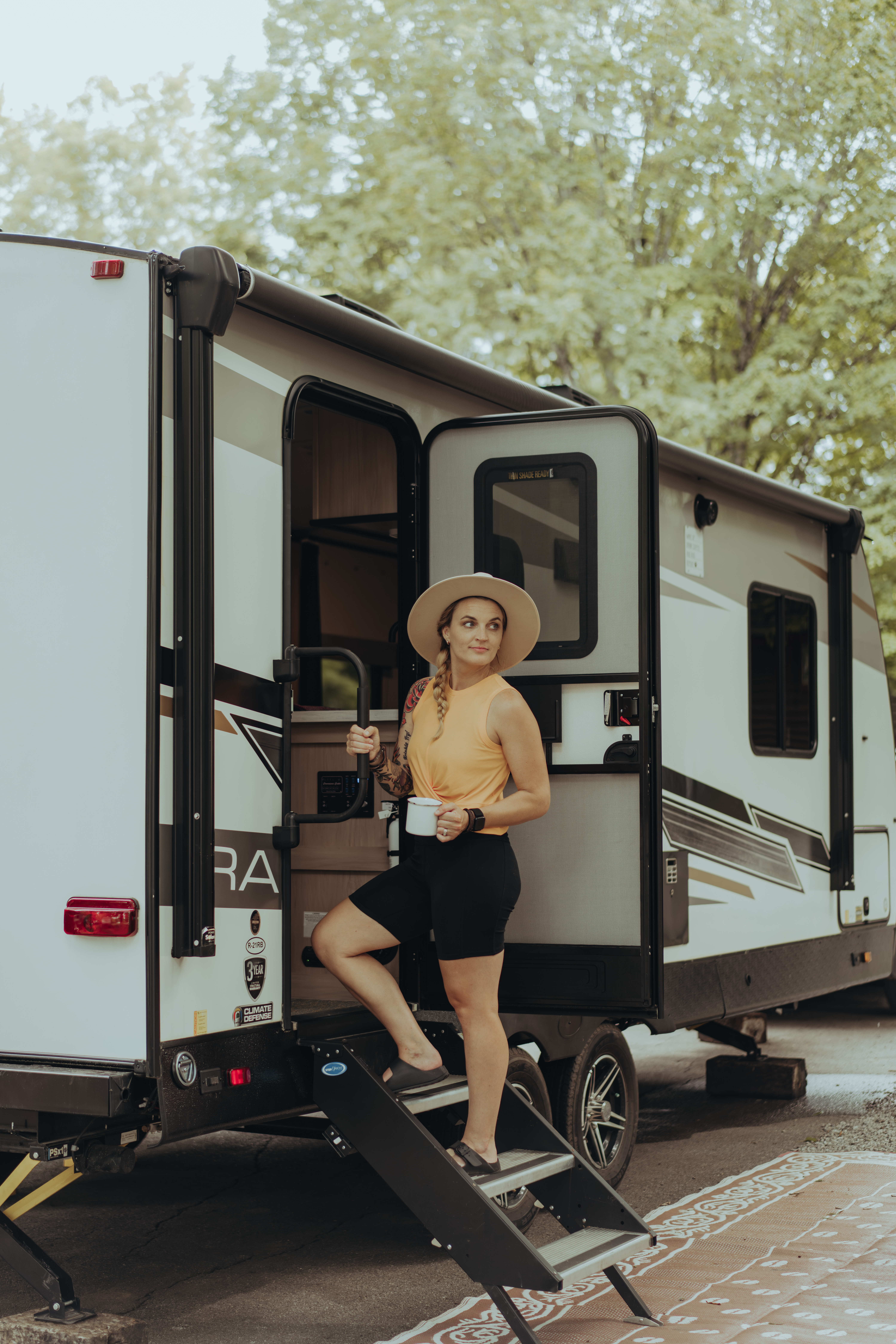 A woman walks up the steps into her travel trailer, smiling