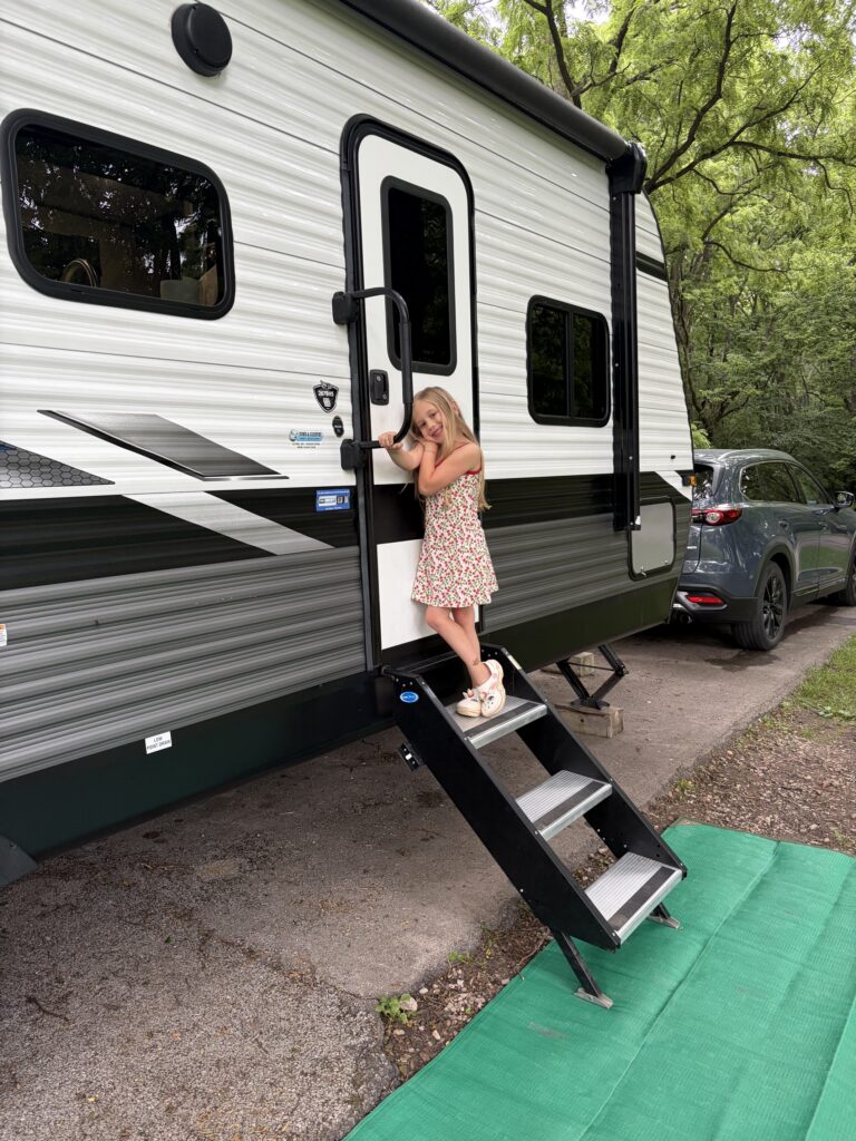 little girl on the steps of a travel trailer, smiling next to the door