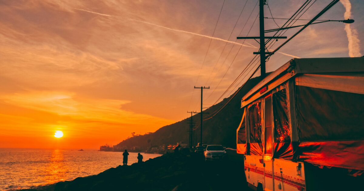 A pop-up trailer along a waterfront with a setting sun