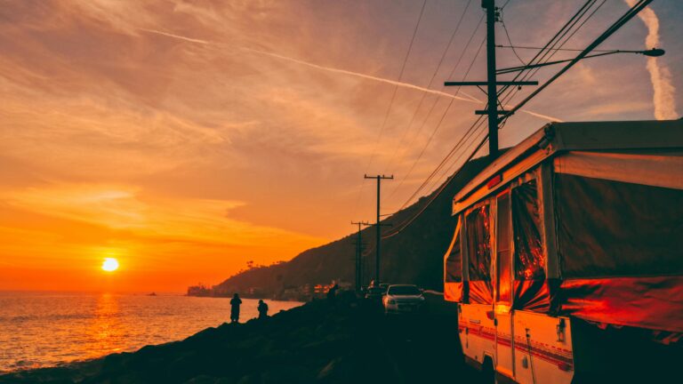 A pop-up trailer along a waterfront with a setting sun