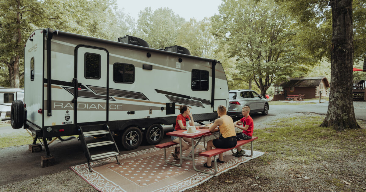 A family sits outside of their travel trailer at a campground, having a good time