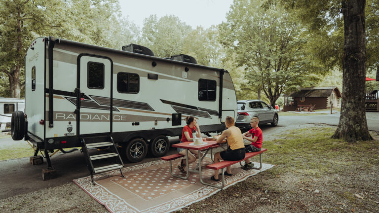 A family sits outside of their travel trailer at a campground, having a good time